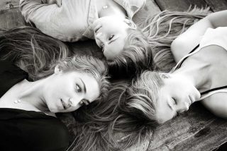 Black and white photography of three sisters with long hair lying down in a circle.