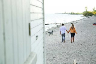 A couple walking on the beach in Toronto with their pet, getting their candid photographs taken.