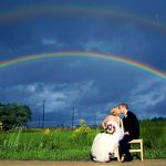 Wedding photography of a couple kissing with a double rainbow in the background.