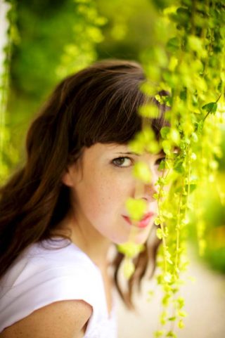 Woman in white dress photograph behind an overhanging plant.